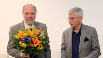 Wolfgang Hackbusch mit einem Blumenstrauß in der Hand, daneben Thomas Höllmann