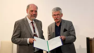 Thomas Höllmann übergibt Wolfgang Hackbusch eine Urkunde