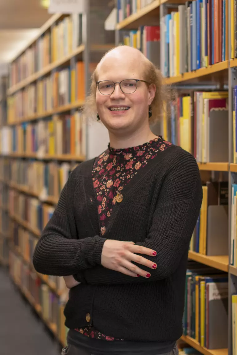 Portrait of Leonie Kayser with folded arms in front of bookshelves