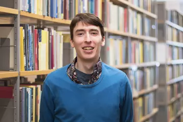 Portrait of Sam G. Krupa smiling in front of bookshelves