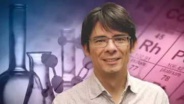 Portrait of Guillermo Restrepo with some flasks and a close-up of the periodic table in the background