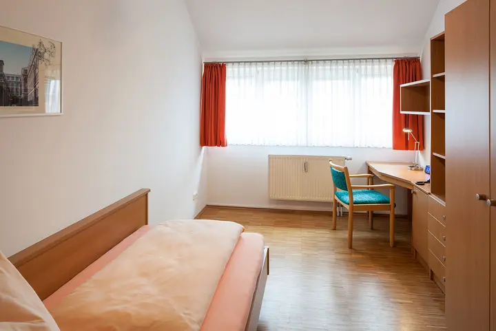 Bedroom with bed, desk, cabinets and a big window.