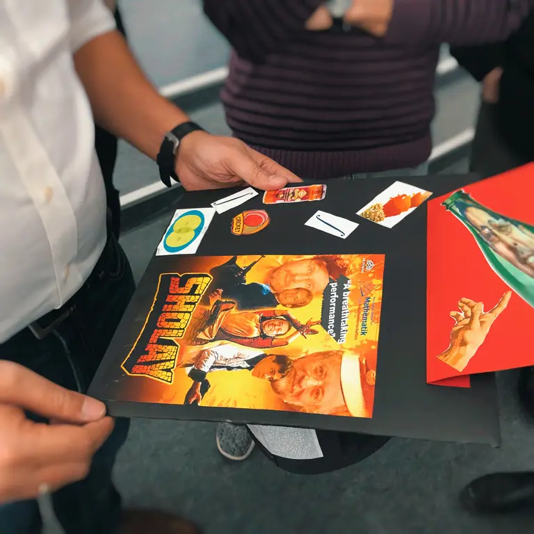 A doctoral cap with various stickers, mainly the cover picture of the movie "Sholay", where the faces of the main characters are replaced by the faces of Pradeep Banerjee, Guido Montúfar, Jürgen Jost and Eckehard Olbrich