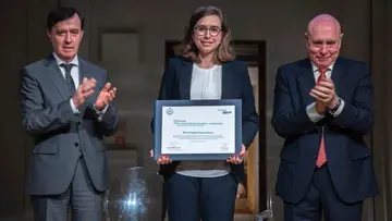 María Ángeles García-Ferrero holds the award certificate. Next to her are two men who are applauding her.