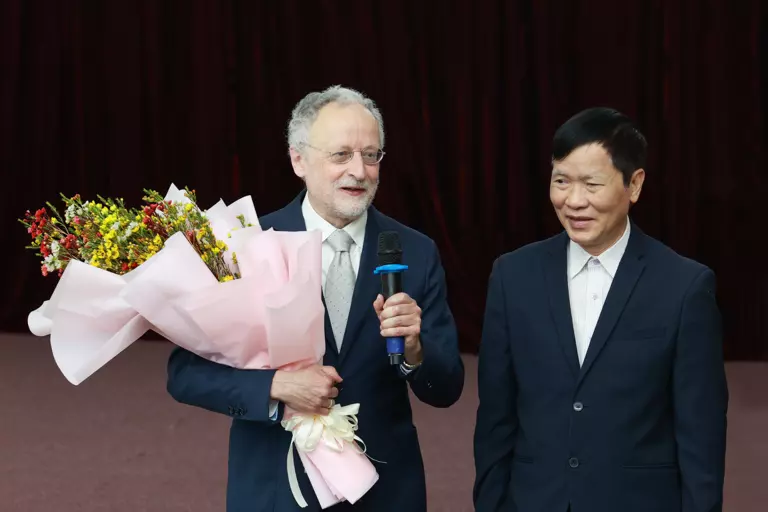 Jürgen Jost is giving a speech, he is holding a bouquet of flowers in his hand, and a Vietnamese colleague is next to him