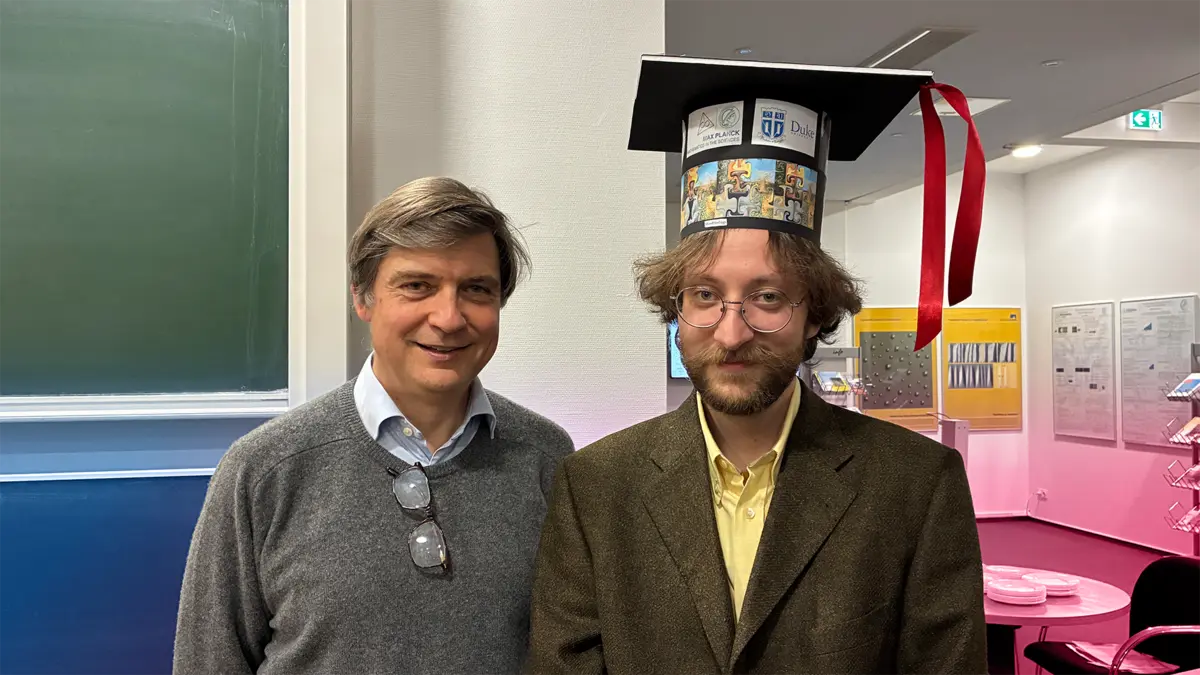 Two people are standing next to each other, smiling (Felix Otto and Konstantin Kalinin). Konstantin is wearing a mortarboard on his head.