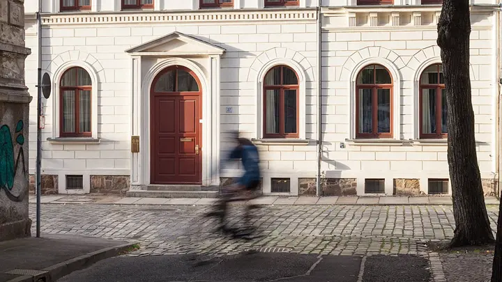 Vorderseite des MPI MiS Gästehauses, rechts ein Baum, ein Fahrradfahrer fährt durchs Bild