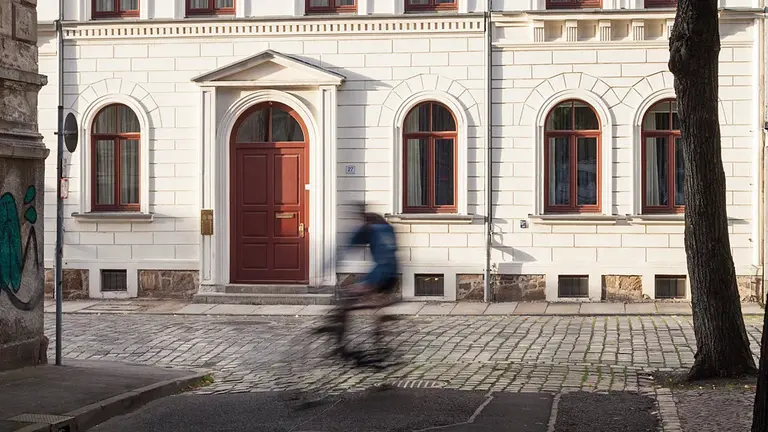 Vorderseite des MPI MiS Gästehauses, rechts ein Baum, ein Fahrradfahrer fährt durchs Bild