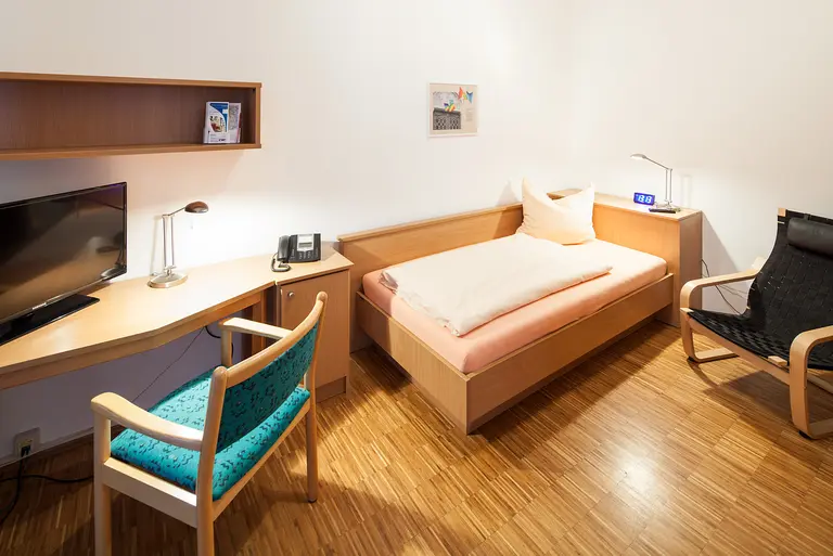 Zimmer mit Bett, Schreibtisch, Stühlen und Fernseher