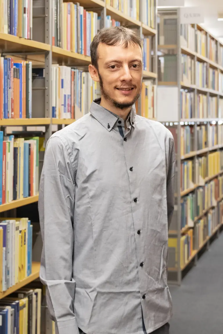 Portrait of Alessio Borzi in front of a bookshelf with one arm behind his back
