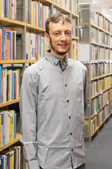 Portrait of Alessio Borzi in front of a bookshelf with one arm behind his back