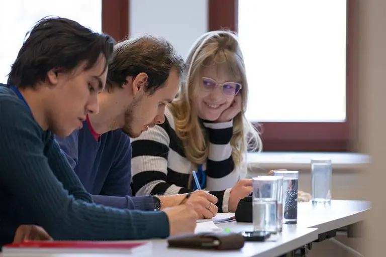 Eine Gruppe von Studierenden sitzt an einem Tisch und tauscht Ideen aus