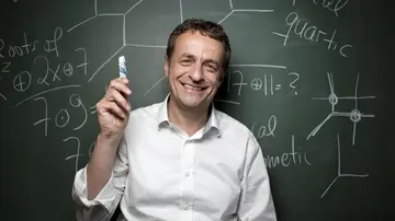 Portrait of Bernd Sturmfels, a blackboard with mathematical formulas in the background