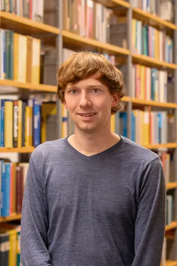 Portrait of Sebastian Bürger in front of bookshelves