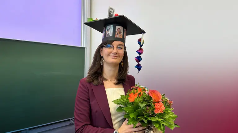 Betti Barbara lächelt in die Kamera. Sie hält einen Blumenstrauss in den Händen und trägt einen Promotionshut.